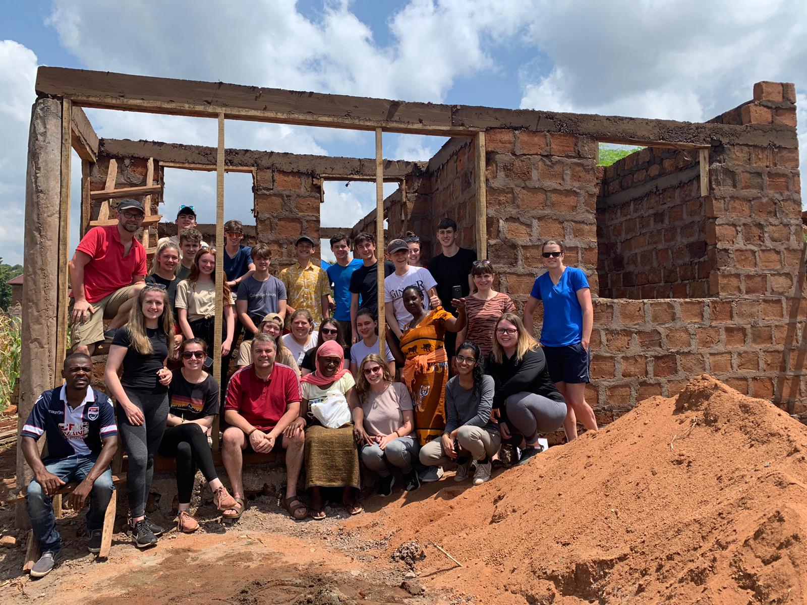 Teacher and students sitting in front of a house being built 